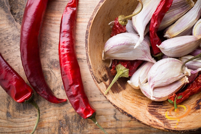 Red cayenne peppers and garlic cloves in a wooden bowl on a rustic surface